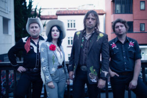 Members of Jenny Don't and the Spurs stand outside in front of a balcony railing.