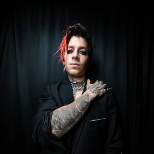 Musician TX2 stands with one of his arm's holding his shoulder.