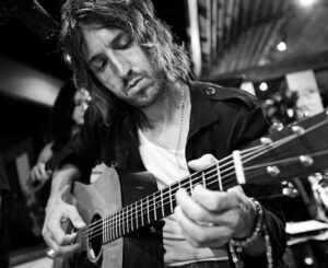 Black and white image of Joseph Arthur playing an acoustic guitar.